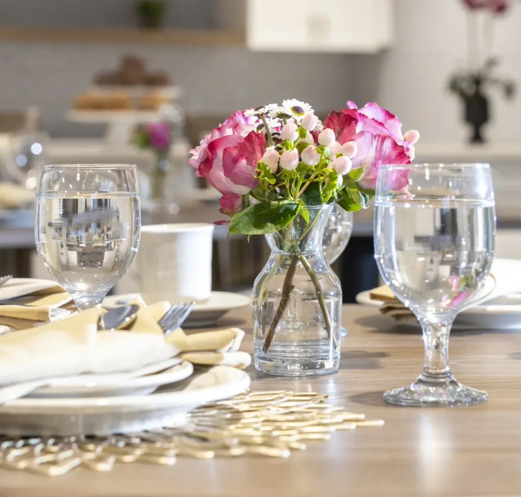 A close-up of an elegantly set dining table in Greenfield, Indiana, with a pink and white floral centerpiece in a glass vase, glassware, and cream-colored napkins.